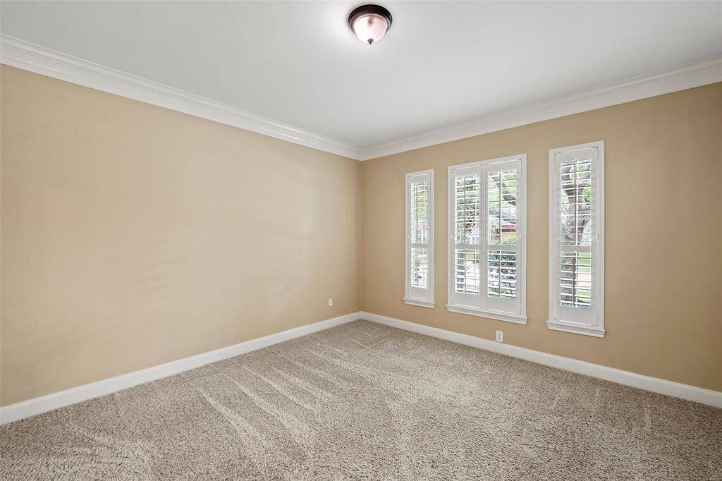 This study/office/5th bedroom features neutral walls, plush carpet, and ample natural light from three tall windows with shutters. Crown molding adds a touch of elegance.