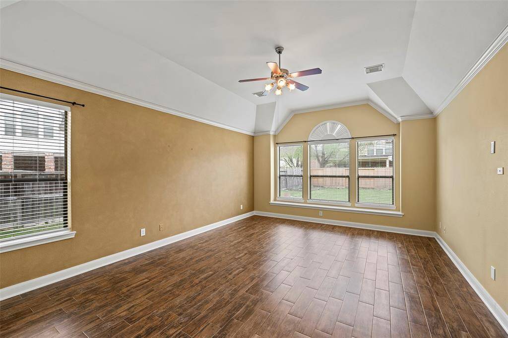 This spacious primary bedroom features warm-toned walls, tile flooring, and large windows that provide ample natural light. The vaulted ceiling with a stylish fan adds a touch of sophistication, making it a welcoming space for relaxation.