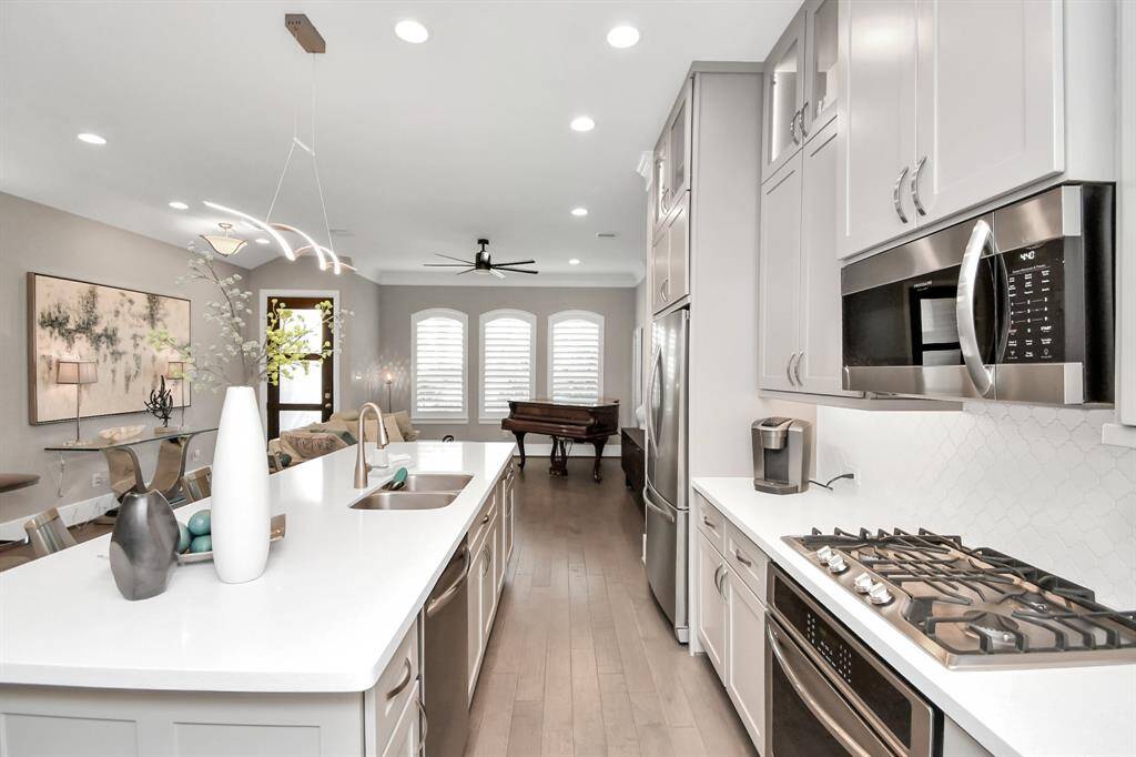 This modern kitchen features sleek cabinetry, stainless steel appliances, and a spacious island with a sink. The open layout flows into a dining area with elegant lighting and large windows, creating a bright and inviting space.