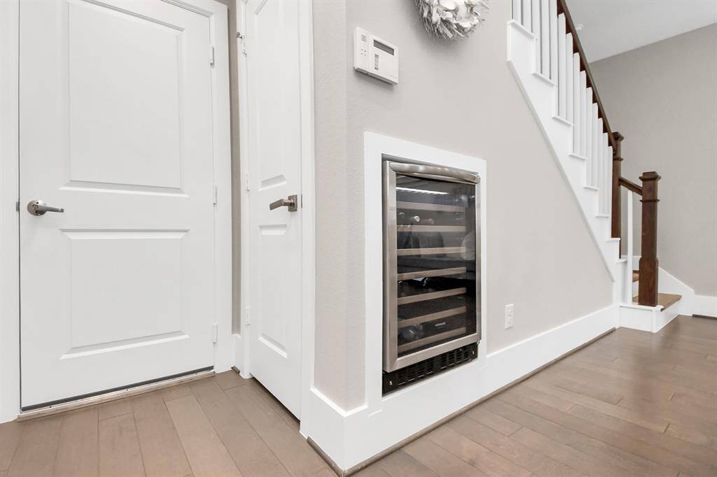 This photo features a modern hallway with light wood flooring, a built-in wine cooler under the stairs, and clean white doors. A staircase with dark wood accents adds elegance to the space.