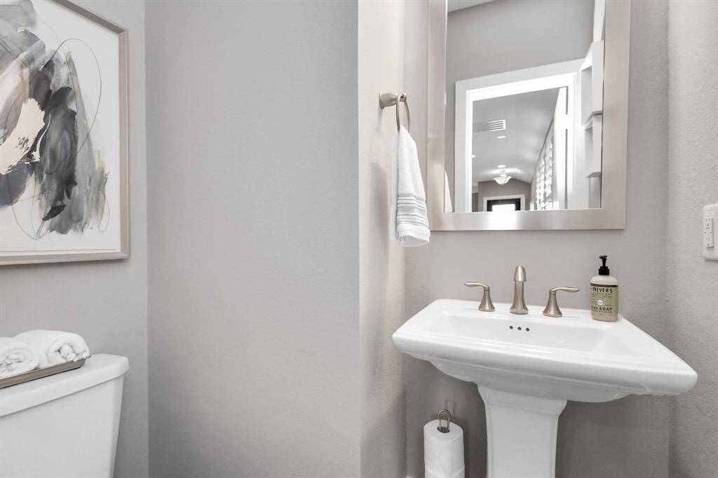This is a modern, compact bathroom with a pedestal sink, stylish mirror, and neutral color palette. It features a towel rack, abstract wall art, and simple decor for a clean, contemporary look.