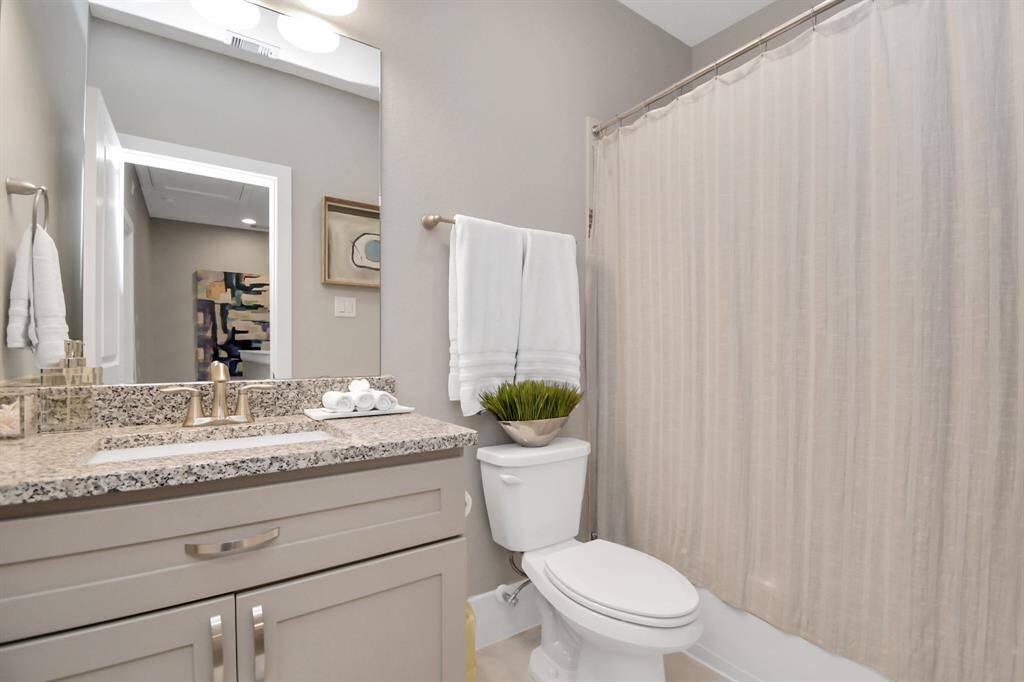 This bathroom features a sleek design with a granite countertop, modern fixtures, and a neutral color palette. It includes a vanity with ample storage, a toilet, and a shower with a curtain. The space is bright and welcoming, perfect for everyday use.