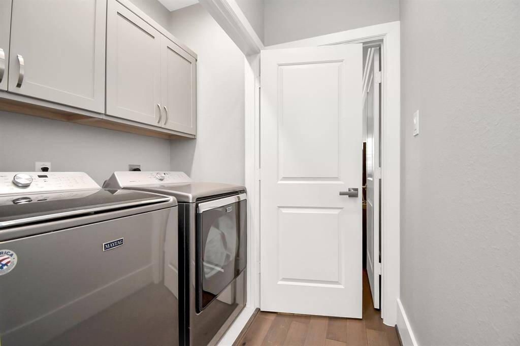 This photo shows a modern laundry room with a washer and dryer, storage cabinets, and a white door. The space is compact and functional, featuring sleek appliances and neutral-colored walls.