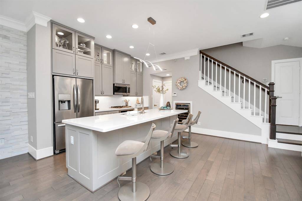 This modern kitchen features sleek gray cabinetry, stainless steel appliances, and a spacious island with seating. The open layout includes a stylish staircase, hardwood floors, and contemporary lighting, creating an inviting and functional space.
