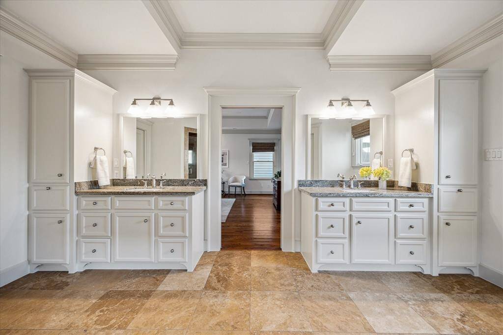 Two separate vanities with linen cabinets provide outstanding storage while travertine tile, designer lighting and crown molding add an elegant touch.
