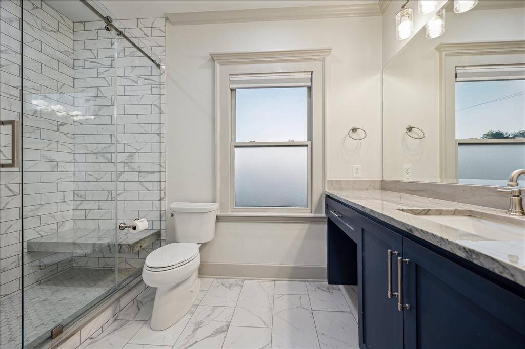 Inside the secondary suite’s newer attached bathroom, you’ll find an oversized glass shower and a lovely blue vanity with a knee space, quartzite counter and contemporary hardware.