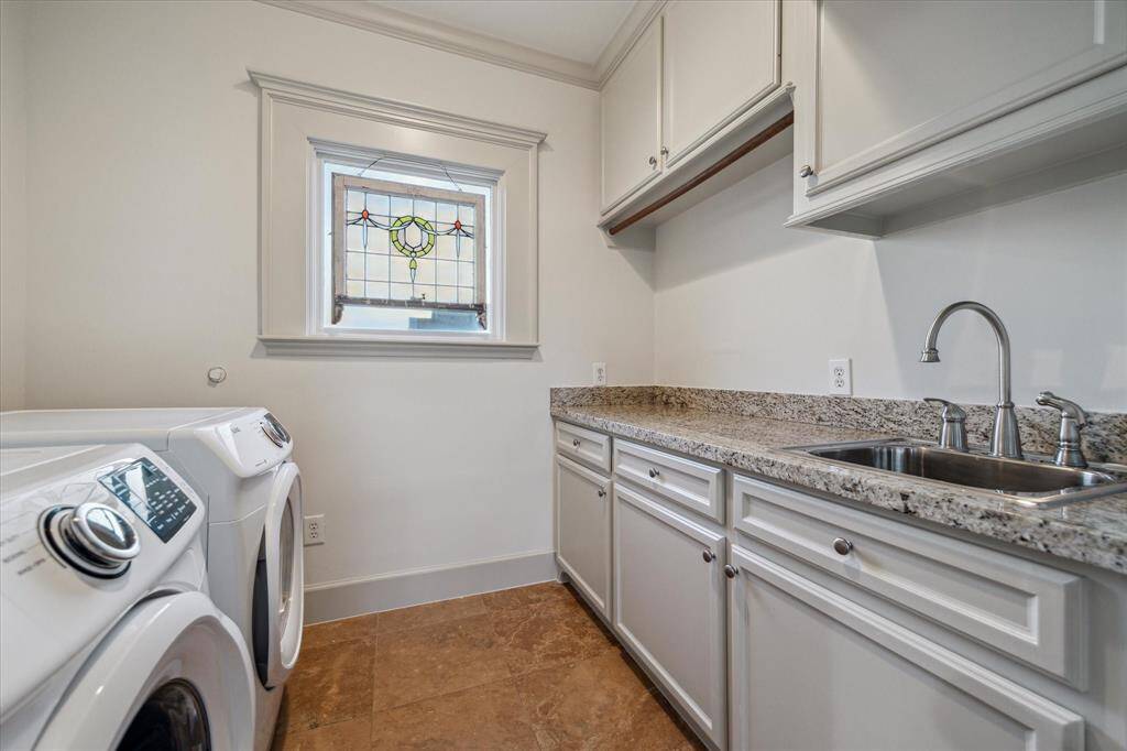 Laundry day is a breeze with this extra-large laundry room appointed with rows of cabinetry, granite folding counter, sink, hanging rod, and both gas and electric connections.