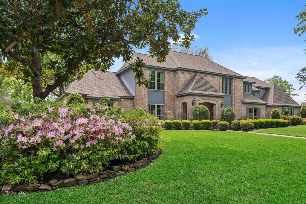 Original owners! Beautiful two-story brick home with a well-maintained lawn and vibrant landscaping, including blooming flowers and manicured shrubs. The house features large windows and a classic architectural style.