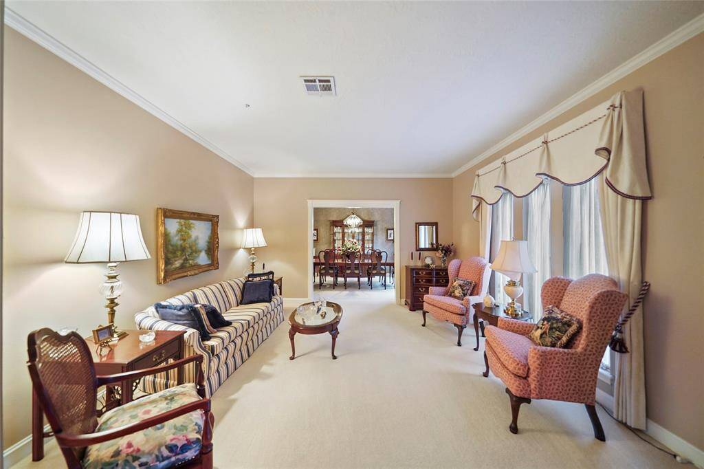 This cozy living room features soft, neutral walls, elegant crown molding, and ample natural light through large windows creating a welcoming atmosphere. The room opens into a formal dining area, offering a seamless flow for entertaining.
