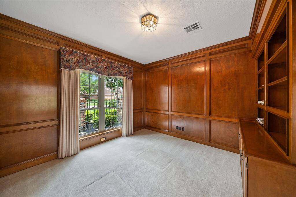 This room features rich wood paneling, built-in shelves, and a large window with drapes, offering a cozy and elegant space ideal for a study or home office.