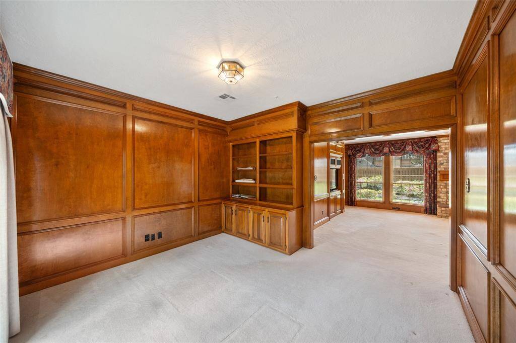 This room features elegant wood paneling, built-in shelves, and an open entryway leading to a bright space with large windows and a view of the garden. Ideal for a cozy library or home office.