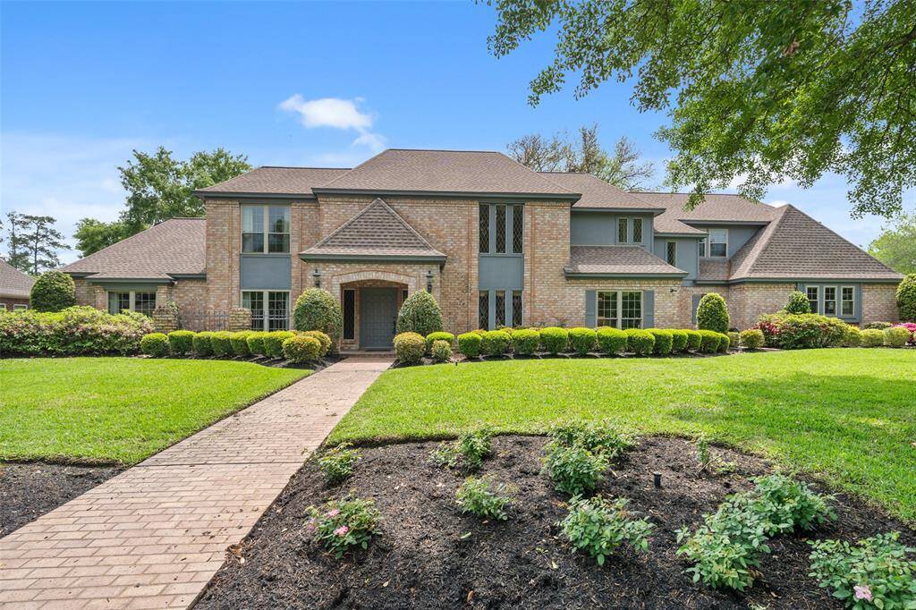 Well-manicured lawn features a symmetrical facade with large windows and a welcoming entrance walkway. The property is surrounded by mature trees, offering a serene and private setting.