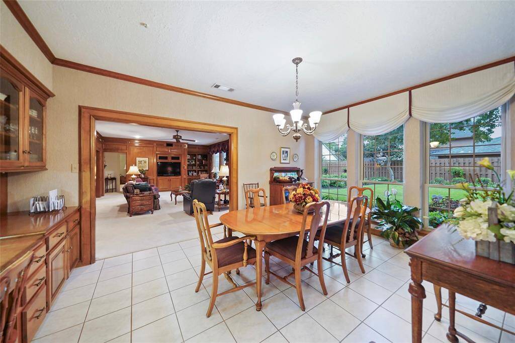 Bright breakfast room area with large windows offering garden views. Adjacent is a cozy living room with wood paneling and built-in shelving, creating a warm, inviting atmosphere.