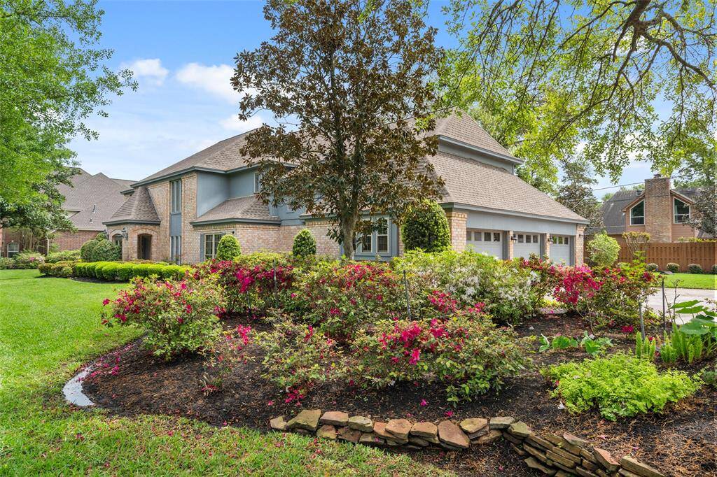 Spacious three-car garage and is surrounded by lush landscaping with vibrant flowering shrubs and mature trees, providing excellent curb appeal.