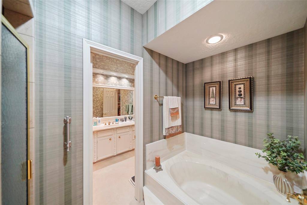 Bathroom featuring a large built-in bathtub with elegant fixtures. Well-lit separate vanity areas with ample counter space, creating a luxurious and inviting atmosphere.