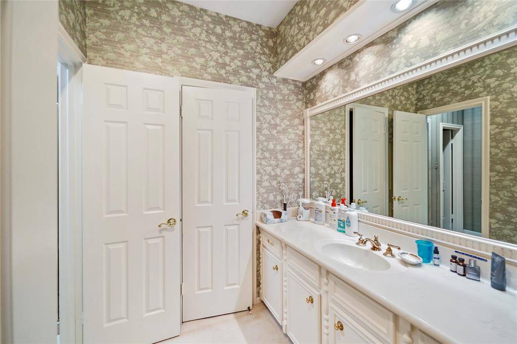Spacious vanity with elegant brass fixtures and ample cabinet storage. Large mirror and decorative wallpaper for a classic look.