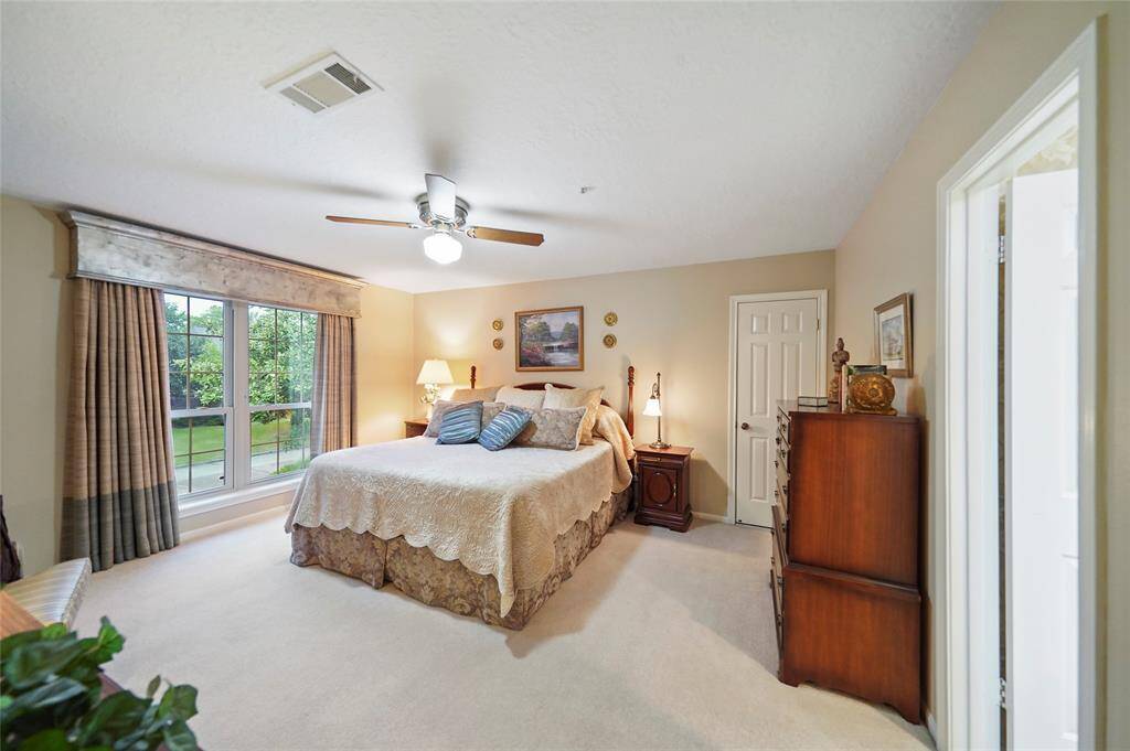 This spacious master bedroom features a large window with a garden view, neutral walls, and cozy carpeting. It includes a ceiling fan, ample natural light creating a warm and inviting atmosphere.