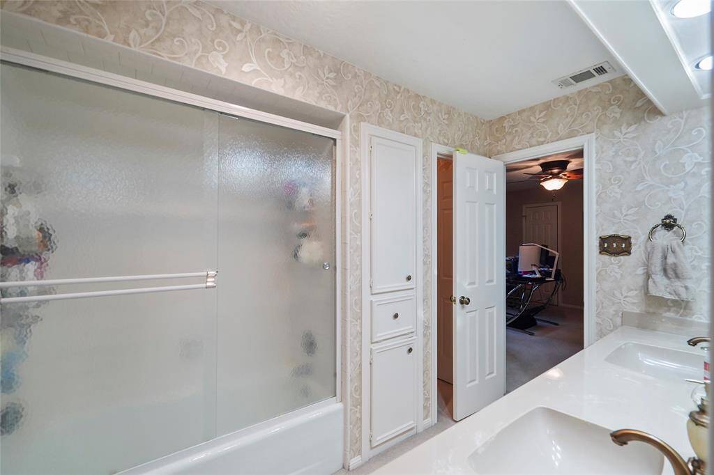 Upstairs secondary bathroom features dual sinks with a wide countertop, a frosted glass shower door, and ornate wallpaper.