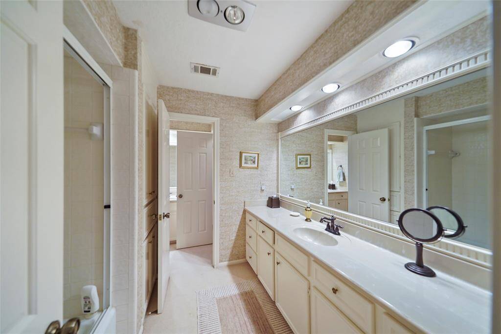This bathroom features an extended vanity with ample storage, a large mirror, and recessed lighting. Custom cabinetry with a walk-in shower.