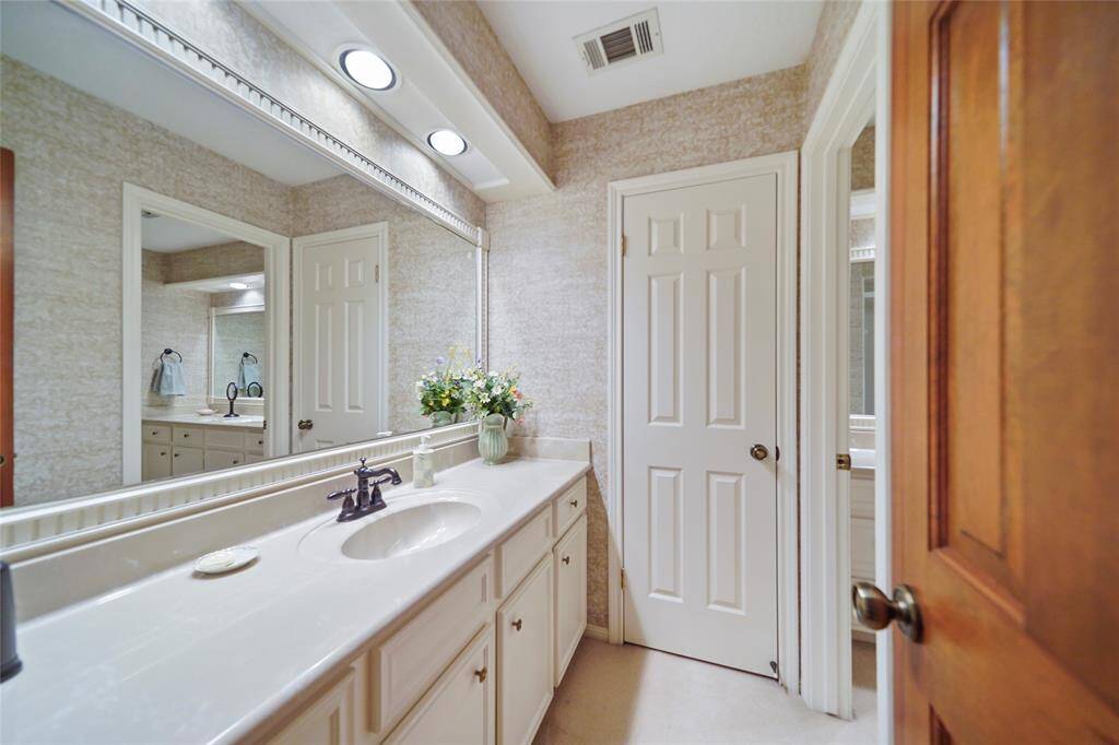 This bathroom features a long vanity, large mirror, and ample storage. It has neutral tones, recessed lighting creating a clean and functional space.