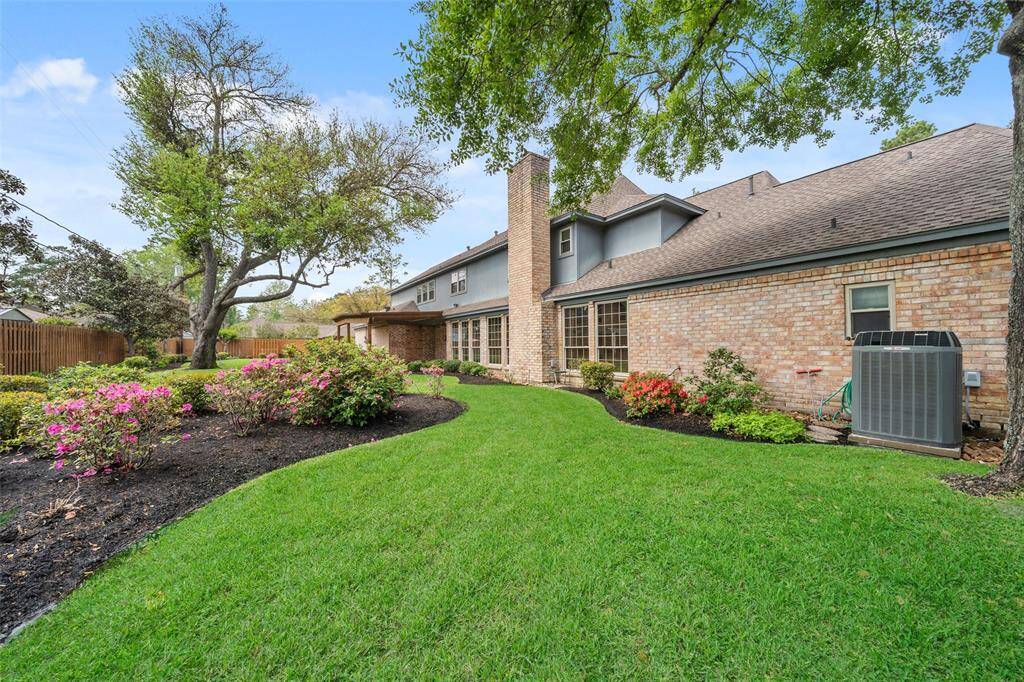 Massive well-maintained backyard. It features lush green grass, colorful flowering shrubs, mature trees, and a cozy patio area creating an inviting outdoor space.