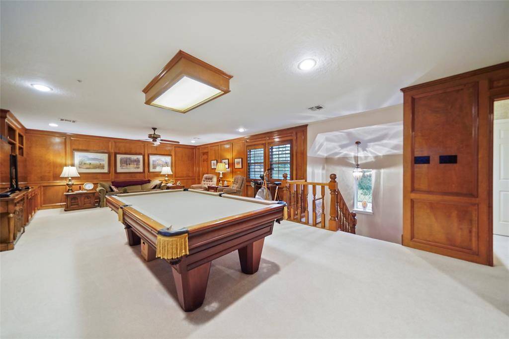 Spacious game room featuring a pool table, cozy seating area, and elegant wood paneling. Ideal for entertainment with ample lighting and a warm, inviting atmosphere.