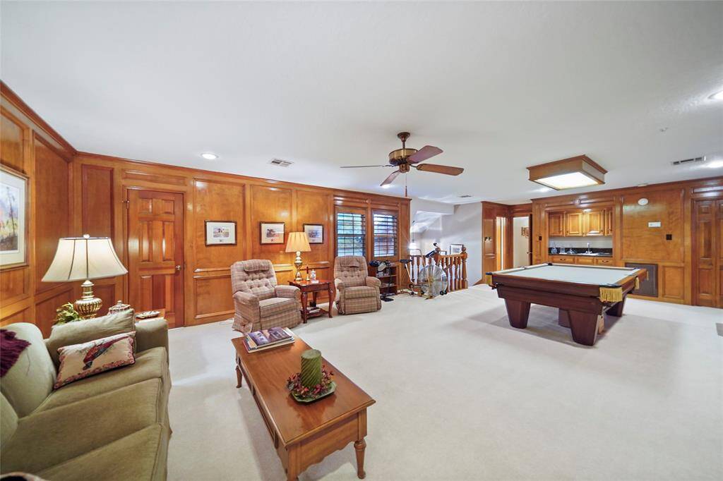 This spacious, wood-paneled living area features a cozy seating space, a pool table, and a mini bar, perfect for entertaining. The room is well-lit and includes ceiling fans, providing a comfortable and inviting atmosphere.