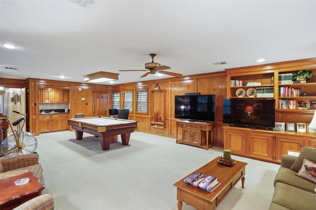 Spacious entertainment room with wood paneling, featuring a pool table, space for large TVs, built-in shelves. Small kitchenette adds convenience, making it perfect for gatherings.