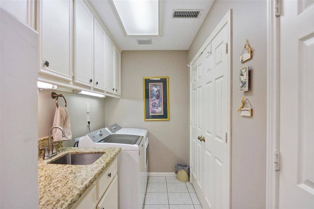 Well-organized laundry room with ample storage. It features granite countertops, a stainless-steel sink, and two closets. The room is bright and functional, with upper cabinets.