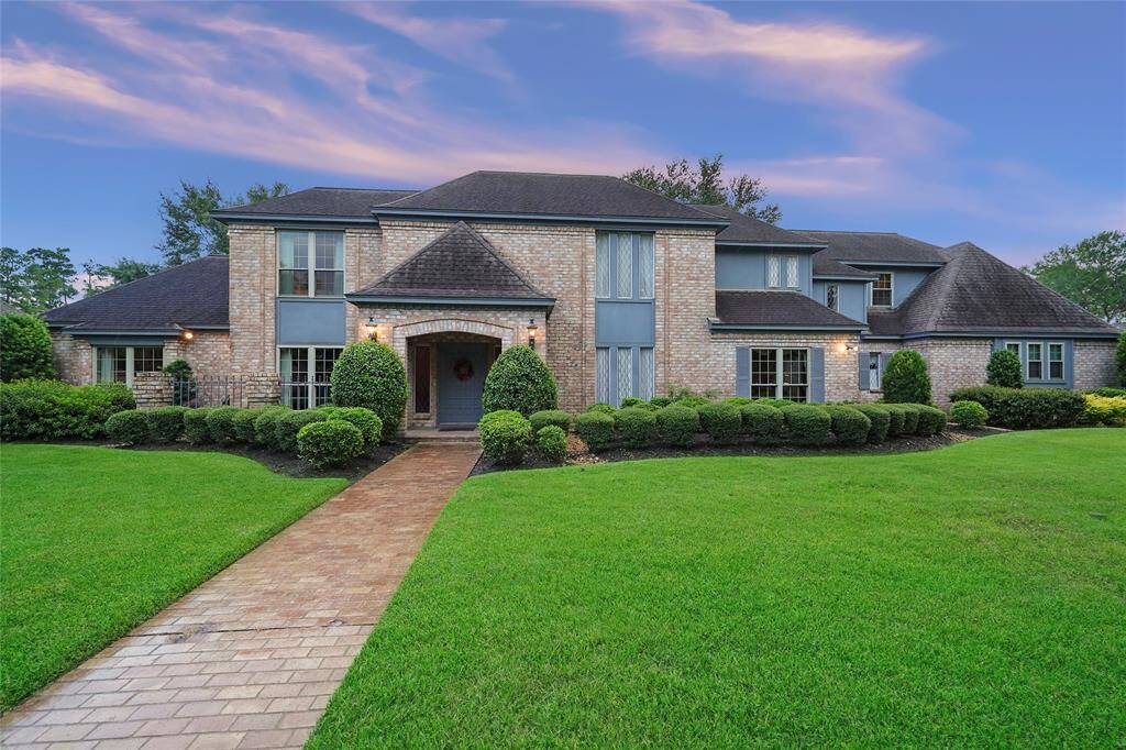 Impressive brick home with a well-maintained lawn and manicured shrubs. The property features multiple gables and a welcoming front pathway.