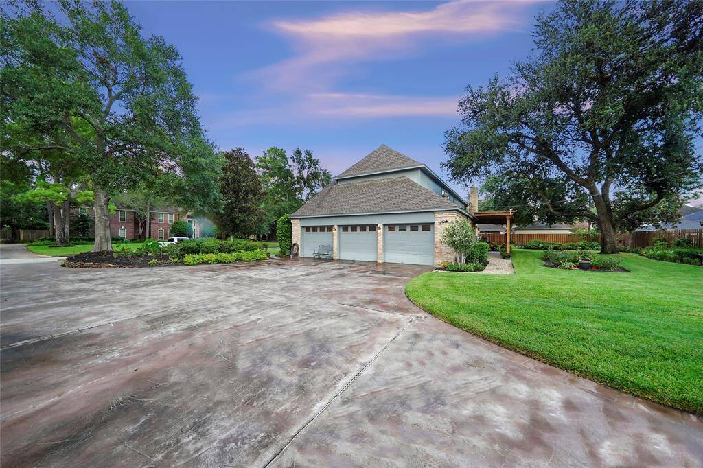 Spacious side-entry driveway leading to a three-car garage, surrounded by lush greenery and mature trees, offering an inviting and well-maintained exterior.