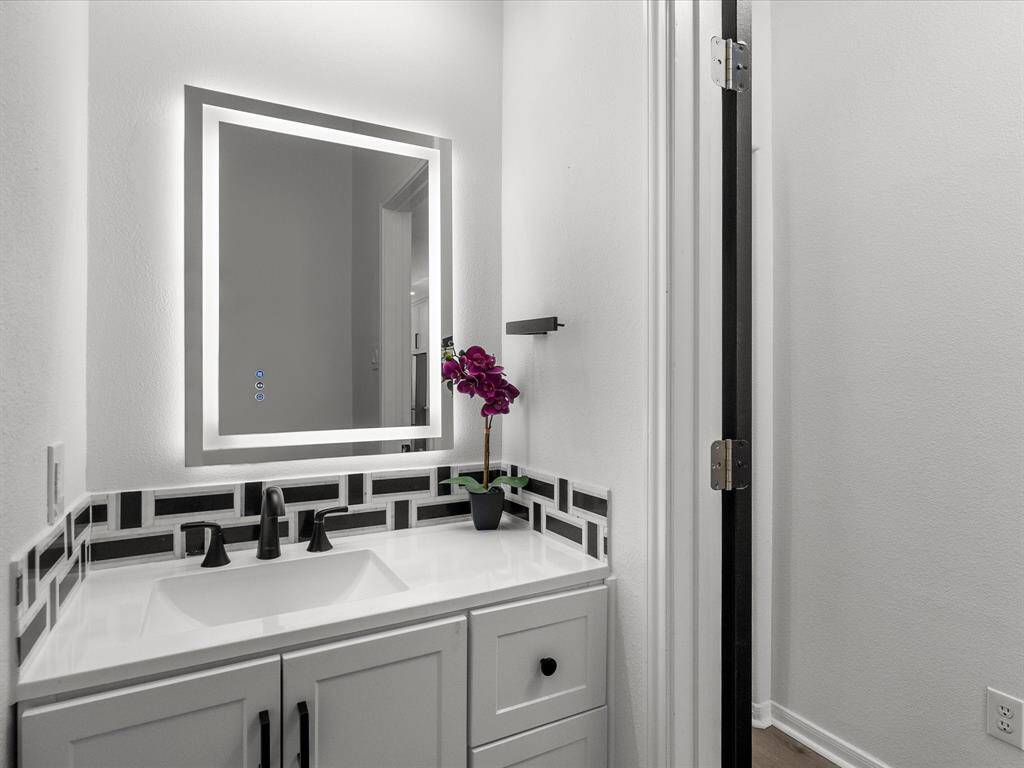 The downstairs half bathroom features a modern vanity with a sleek, illuminated mirror, stylish black fixtures, and a decorative backsplash.