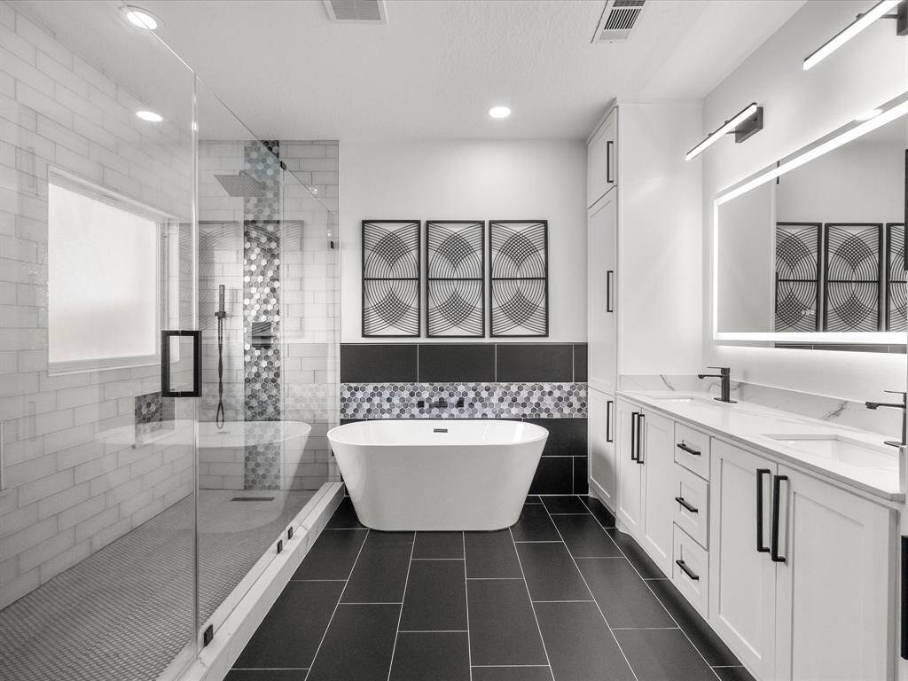 Modern primary en-suite features a sleek freestanding tub, an extremely spacious glass-enclosed shower, and elegant black tile flooring. Ample cabinetry and a large vanity provide plenty of storage, while the minimalist design and neutral color palette create a serene atmosphere.