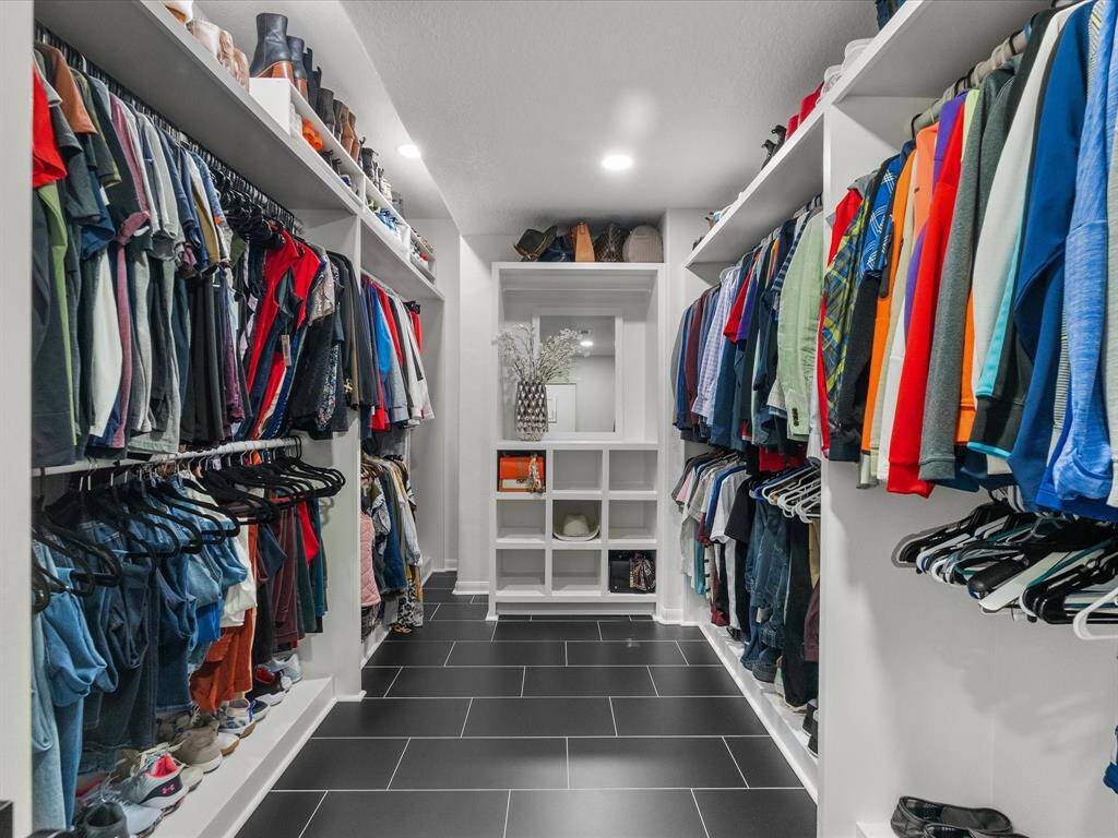 Spacious walk-in closet with ample hanging space, shelving for shoes and accessories, and continuous modern black tile flooring.