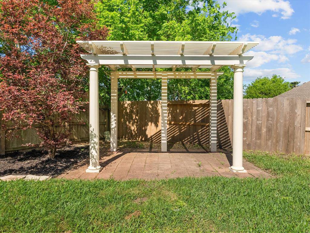 This backyard features a charming pergola on a stone patio, surrounded by lush greenery and a wooden fence, offering a private and inviting outdoor space.