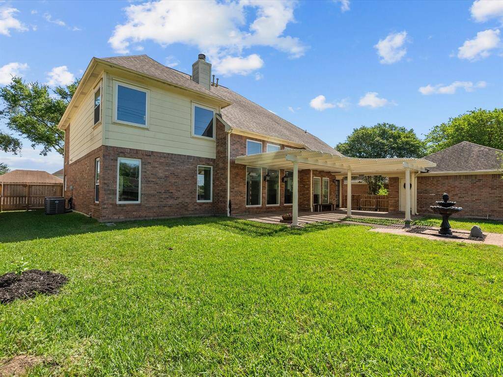 Spacious backyard with a well-maintained lawn, a covered patio with a pergola, and a charming fountain feature.
