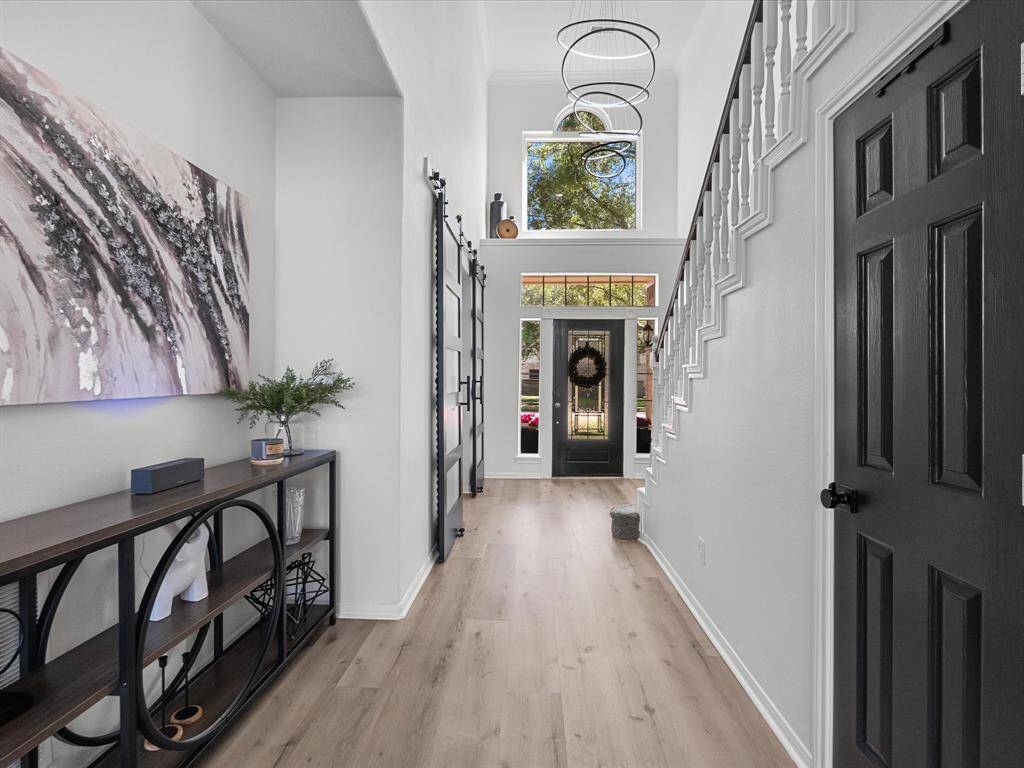 This inviting entryway features high ceilings, a modern chandelier, and abundant natural light. The elegant staircase and stylish decor create a warm, welcoming atmosphere.