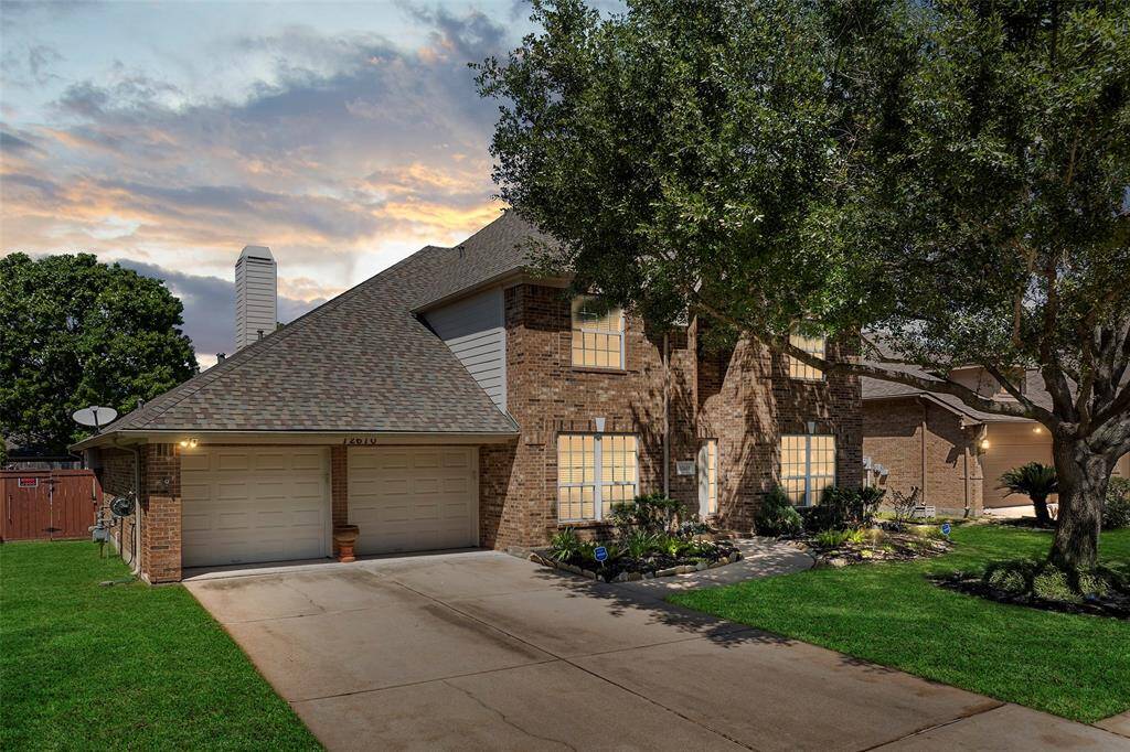 This is a two-story brick house with a two-car garage, well-maintained lawn, and mature trees. The property has a spacious driveway and a welcoming front entrance.