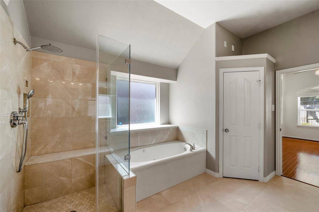 This bathroom features a spacious layout with a dual-sink vanity, large mirror, and modern light fixtures. It includes a glass-enclosed shower and a separate bathtub, complemented by neutral tiles and elegant finishes.
