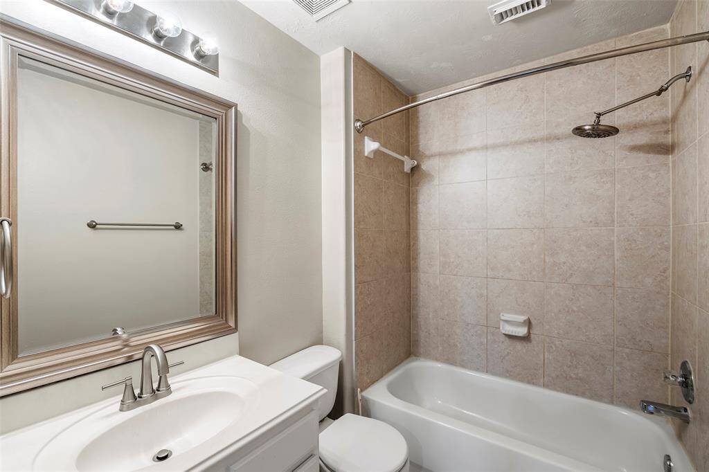 This bathroom features a modern design with a tiled shower and bathtub combo, a sleek vanity with a large framed mirror, and updated fixtures for a clean and functional space.