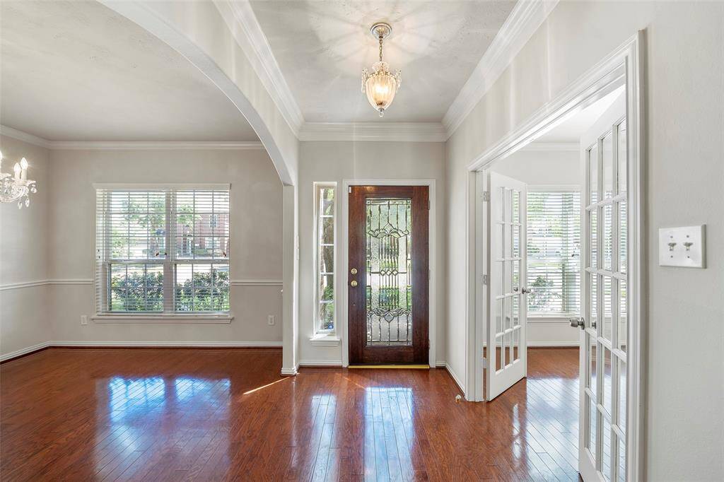 This photo showcases a bright entryway with a decorative glass front door, hardwood floors, and elegant French doors leading to an adjacent room. Large windows allow natural light to fill the space, enhancing its welcoming atmosphere.