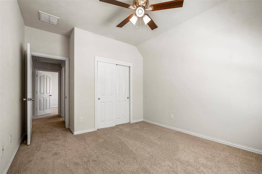 This inviting bedroom boasts neutral walls and carpet, a ceiling fan with lights, and a convenient closet. An open doorway seamlessly connects to a hallway with stairs.