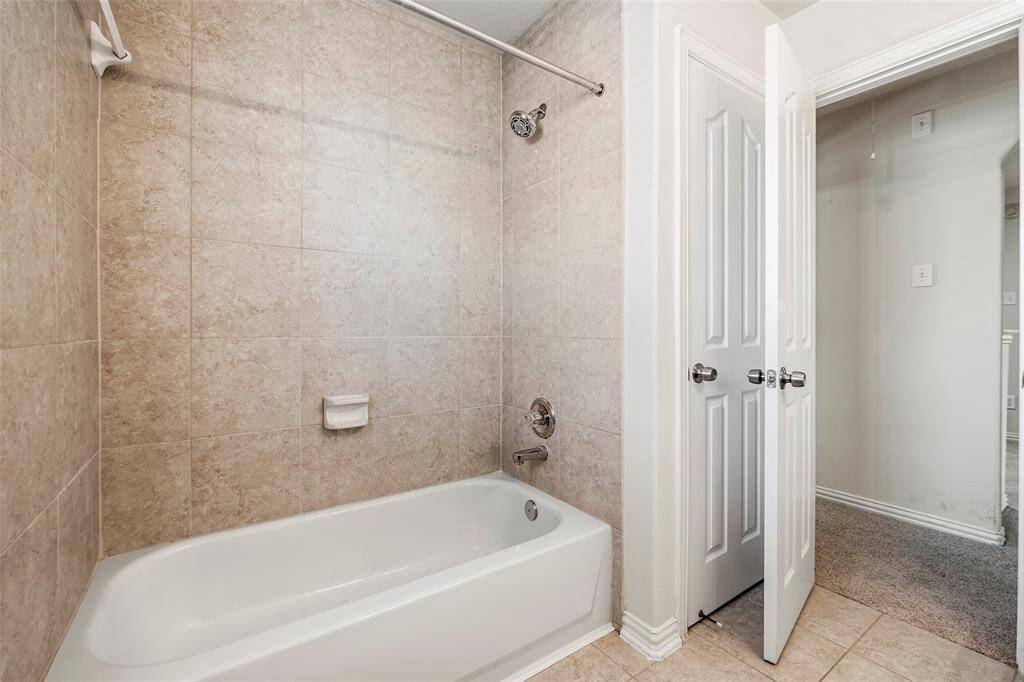 This bathroom features a clean, modern design with a single sink vanity, large mirror, and overhead lighting. It includes a tiled shower area and a window for natural light.