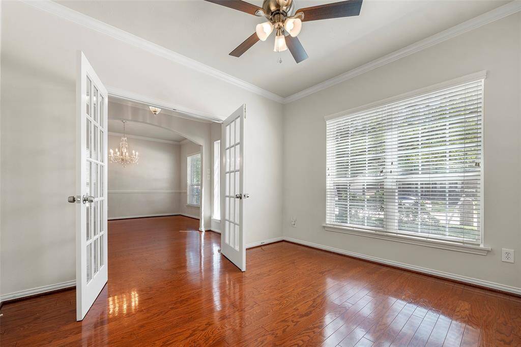 This Home Office features elegant wooden flooring, French doors, and a ceiling fan. Large windows provide plenty of natural light,