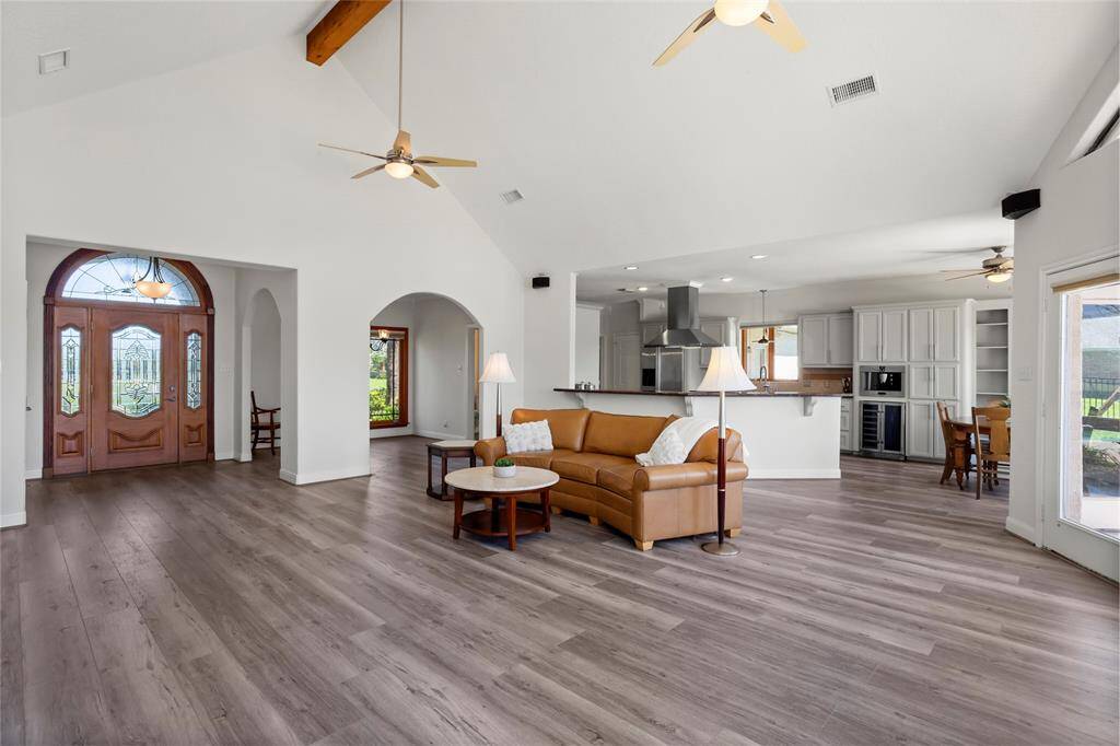 Discover the charm of this open-concept living area with elegant wood flooring, vaulted ceilings, and abundant natural light. The space flows into a modern kitchen featuring gray cabinets and stainless-steel appliances. A grand entrance with a wooden door and decorative glass panels welcomes you home.