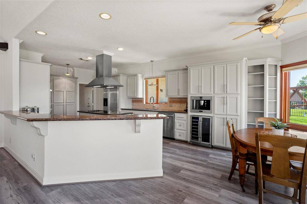 Experience culinary luxury in this modern kitchen featuring sleek cabinetry, a central island with a cooktop and stainless-steel range hood, plus a built-in double oven. Enjoy seamless flow to the breakfast area with stunning backyard views.