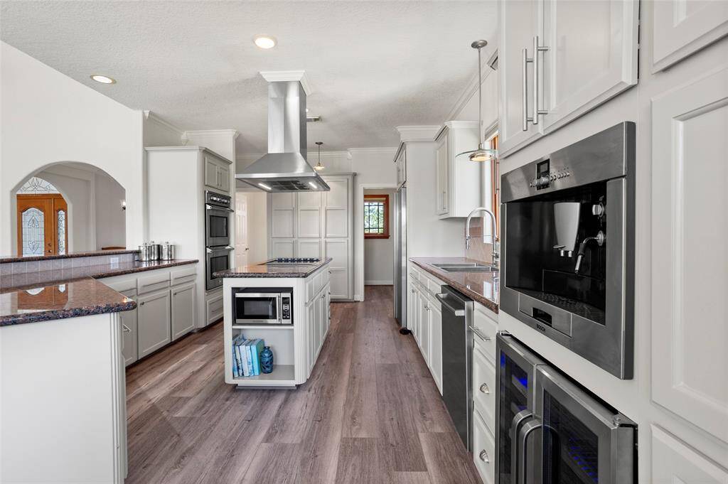 This modern kitchen features sleek cabinetry, stainless steel appliances, and a central island with a cooktop and microwave. Check out the built-in espresso/coffee maker and brand-new wine & beverage fridge.