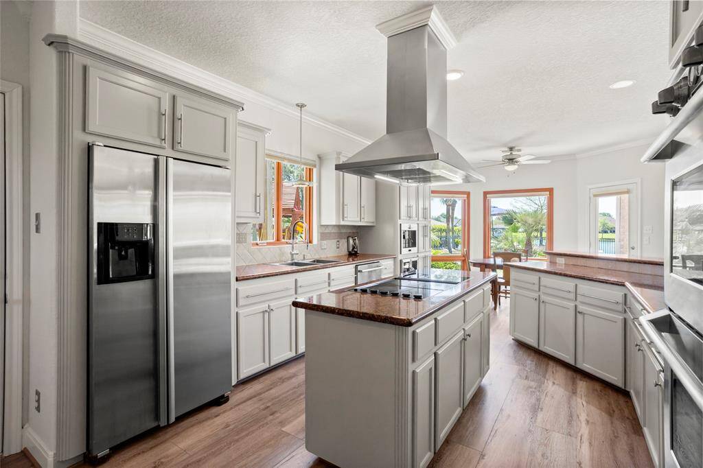 This kitchen features modern stainless-steel appliances, an island with a cooktop and range hood, and ample cabinetry. Large windows provide plenty of natural light and offer a scenic view, while the open layout connects to a dining area and living area.