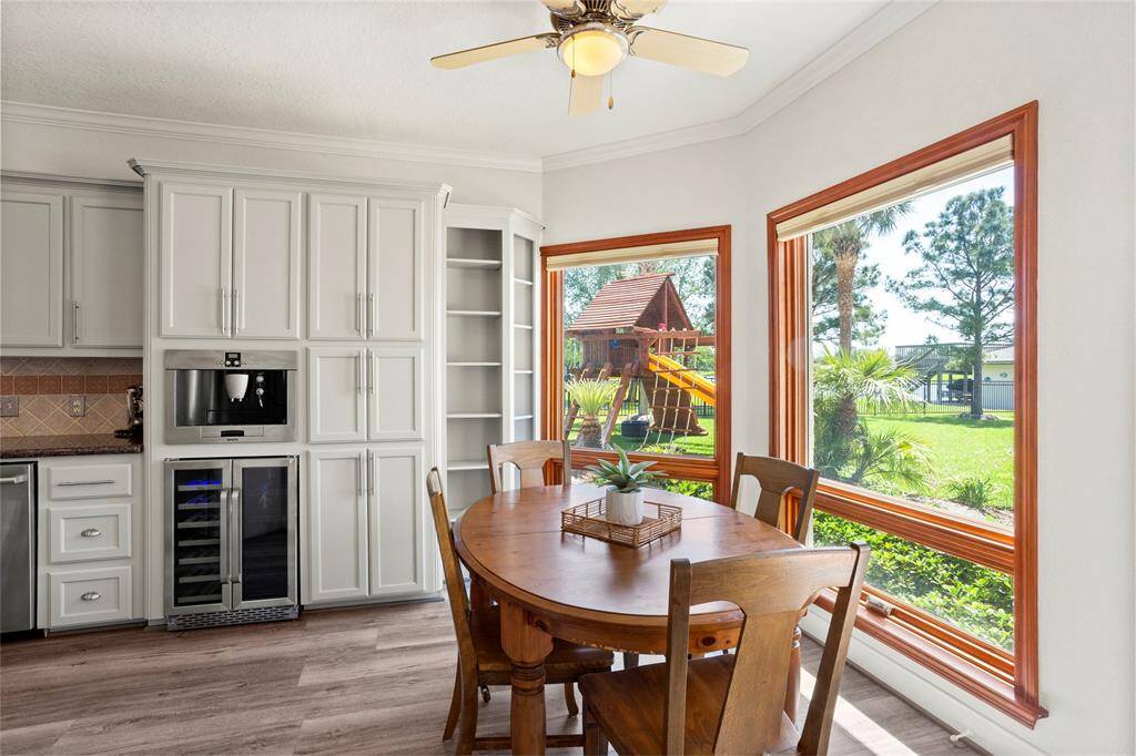 Bright breakfast dining area with large windows overlooking a lush backyard and lake. Features built-in shelving, and modern appliances, including a coffee/espresso machine and wine fridge. Perfect for family meals with great views.