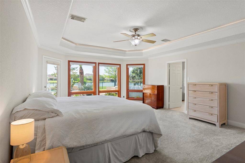 The primary bedroom offers stunning lake and backyard views through large windows, features a tray ceiling with ambient uplighting, and has new carpeting. Enjoy direct access to the backyard through a private door.